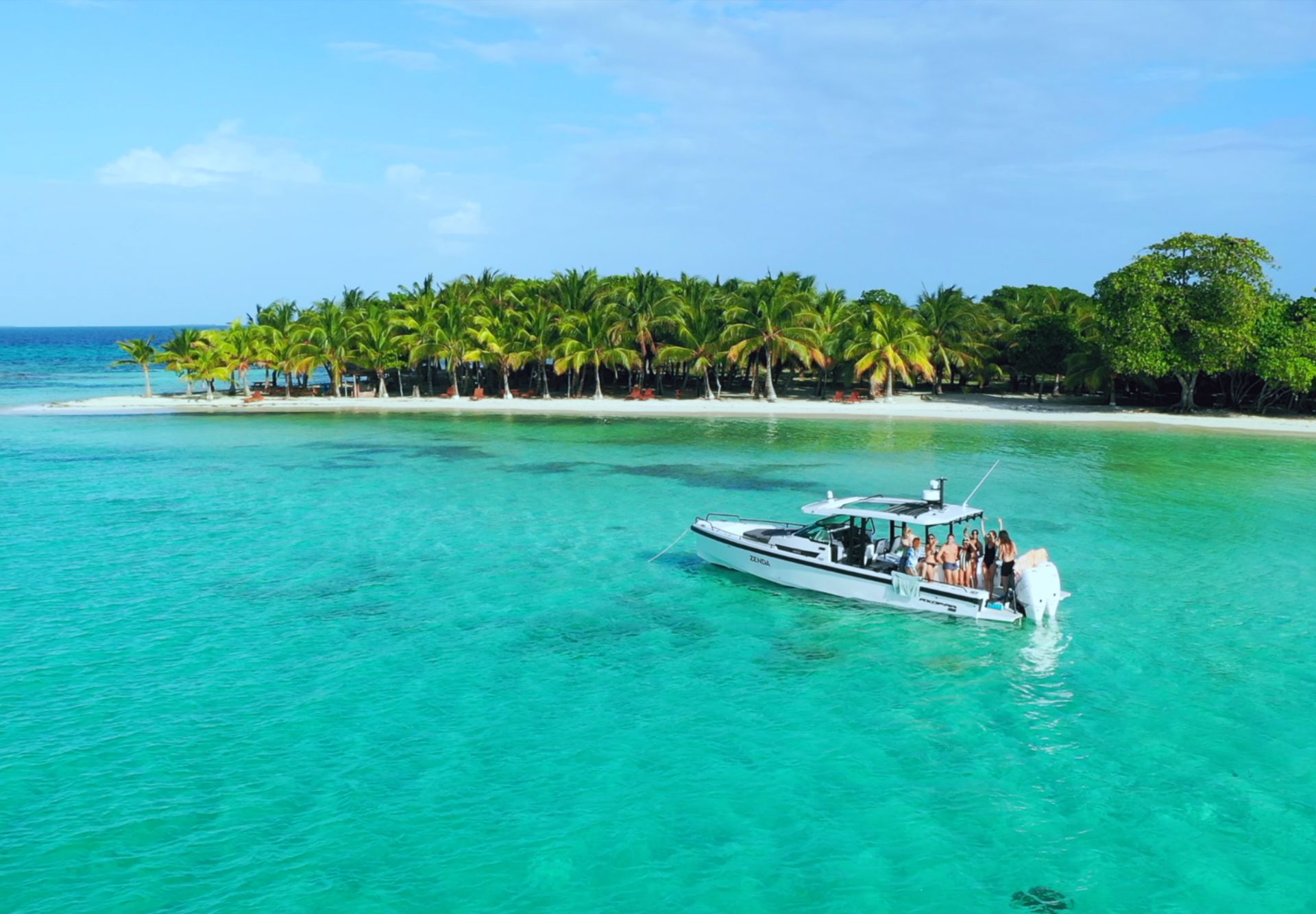 A group aboard a motorboat in turquoise water beside a palm-covered island