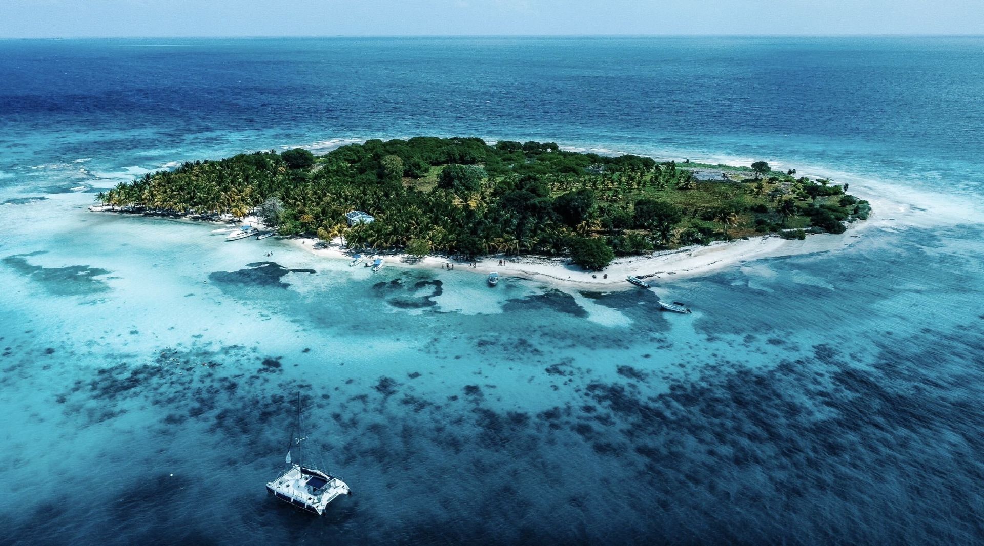 An aerial view of a green island edged by white sand and turquoise reef waters